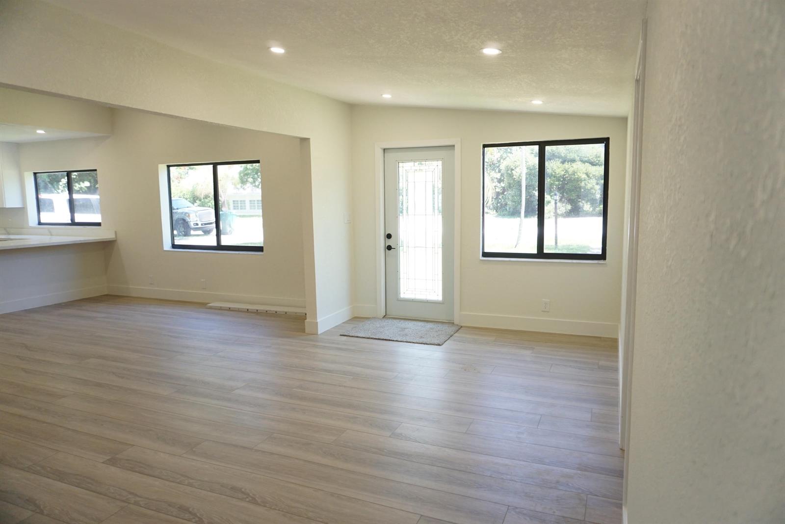 An open-concept living area features light wood-look flooring, white walls, and a front entry door — 310 SW 1st Avenue, Boynton Beach FL 33435, BOYNTON BEACH, FL