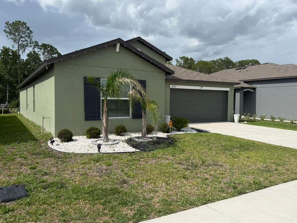 A single-story house with green stucco siding, dark shutters, a two-car garage, and palm trees — 2000 RED LOOP, LAKELAND, FL