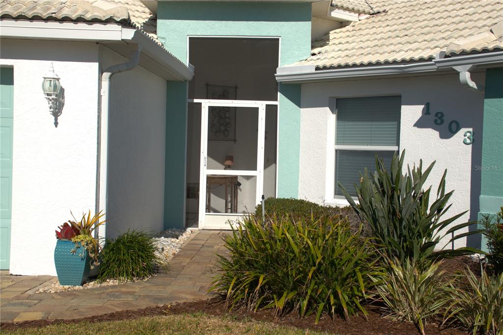 A paved walkway leads to the screened front entryway of a house with light-colored stucco — 1303 ISLAMORADA BOULEVARD, PUNTA GORDA, FL