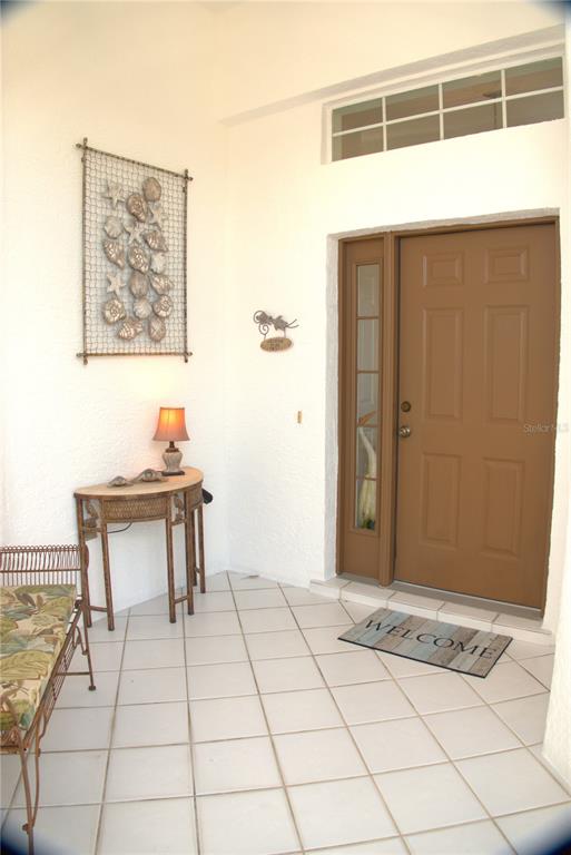 A covered entryway features a brown door, tiled floor, wicker furniture, and coastal wall decor — 1303 ISLAMORADA BOULEVARD, PUNTA GORDA, FL