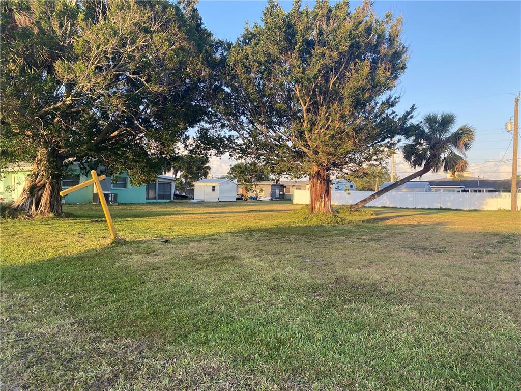 A grassy lot features several large trees, a small shed, and a leaning palm tree — 543 AZALEA DRIVE NW, PORT CHARLOTTE, FL