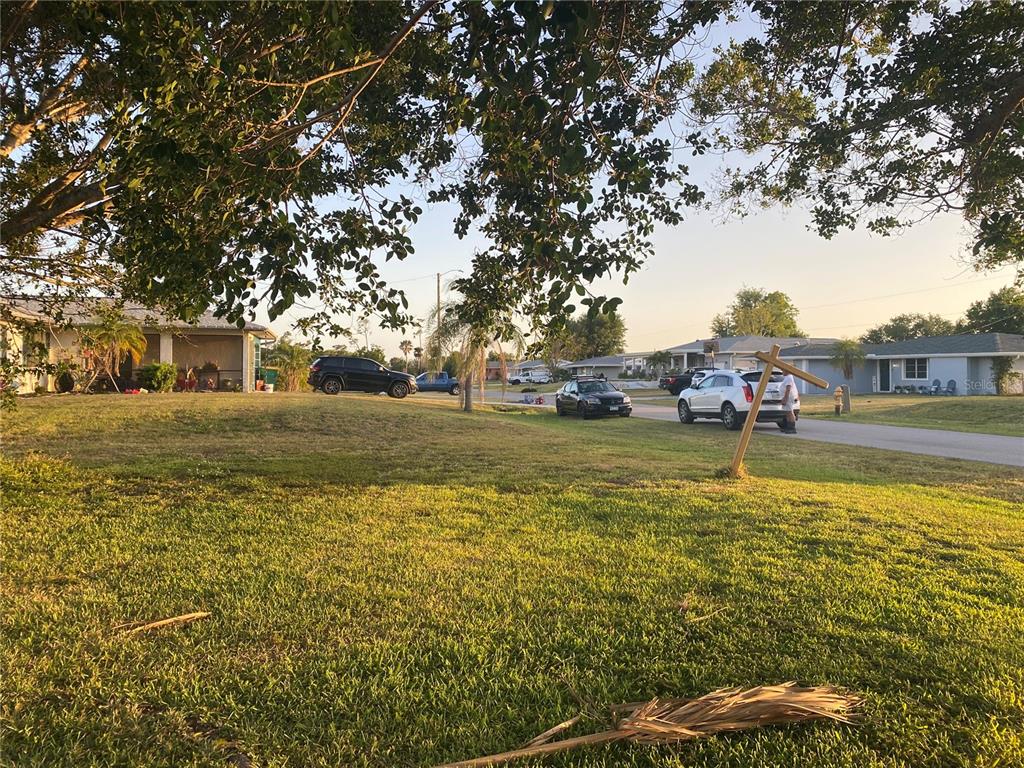 A grassy residential lot with a wooden sign post and several parked cars on the street — 543 AZALEA DRIVE NW, PORT CHARLOTTE, FL