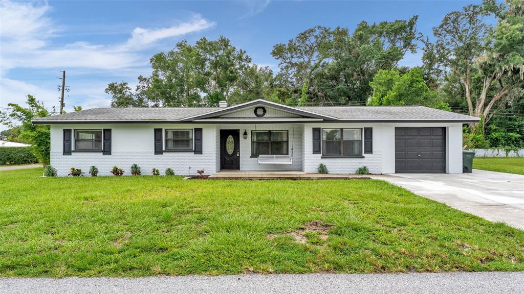 A single-story white brick house with a dark garage door and a front porch swing — 135 KENILWOOD LANE, LAKELAND, FL