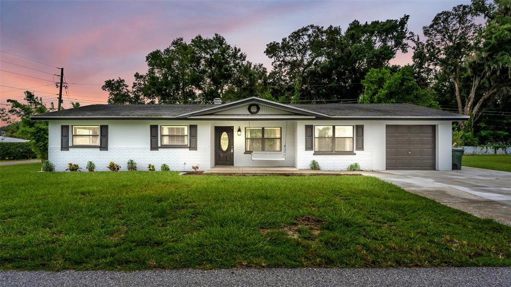 A single-story white brick house with a dark roof, front porch, and attached garage — 135 KENILWOOD LANE, LAKELAND, FL