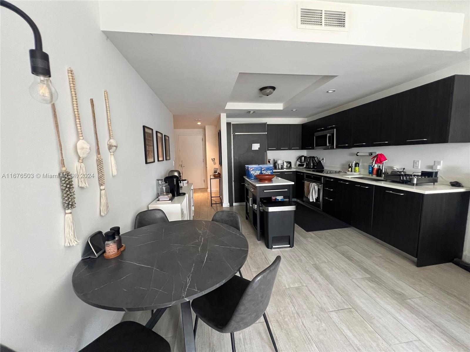 A kitchen and dining area features dark cabinetry, a marble-topped table, and light wood flooring — 55 SW 9th St # 1604, Miami FL 33130, MIAMI, FL