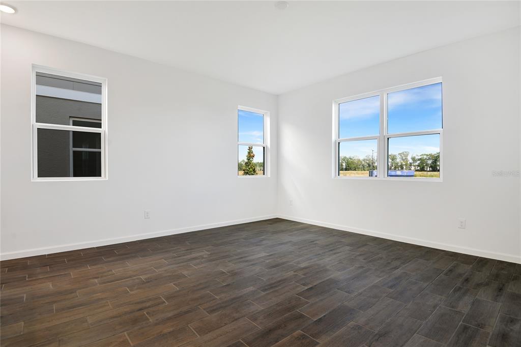 An empty room features white walls, dark wood-look tile flooring, and three windows — 6155 SW 64TH TERRACE, OCALA, FL