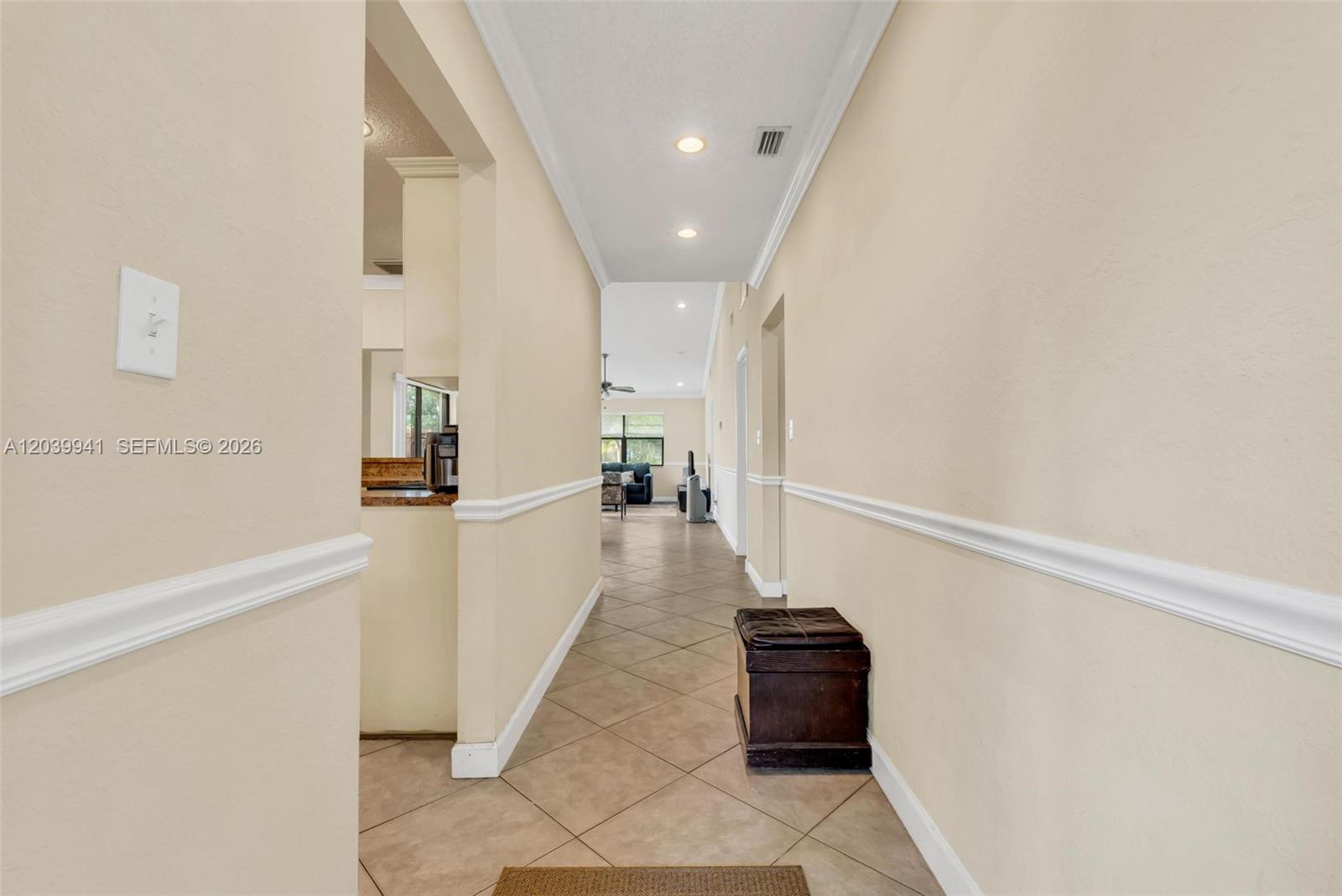 A hallway with beige walls, chair rail molding, and tile flooring leads to a living area — 6633 N Parkway Dr # 7, Margate FL 33068, MARGATE, FL