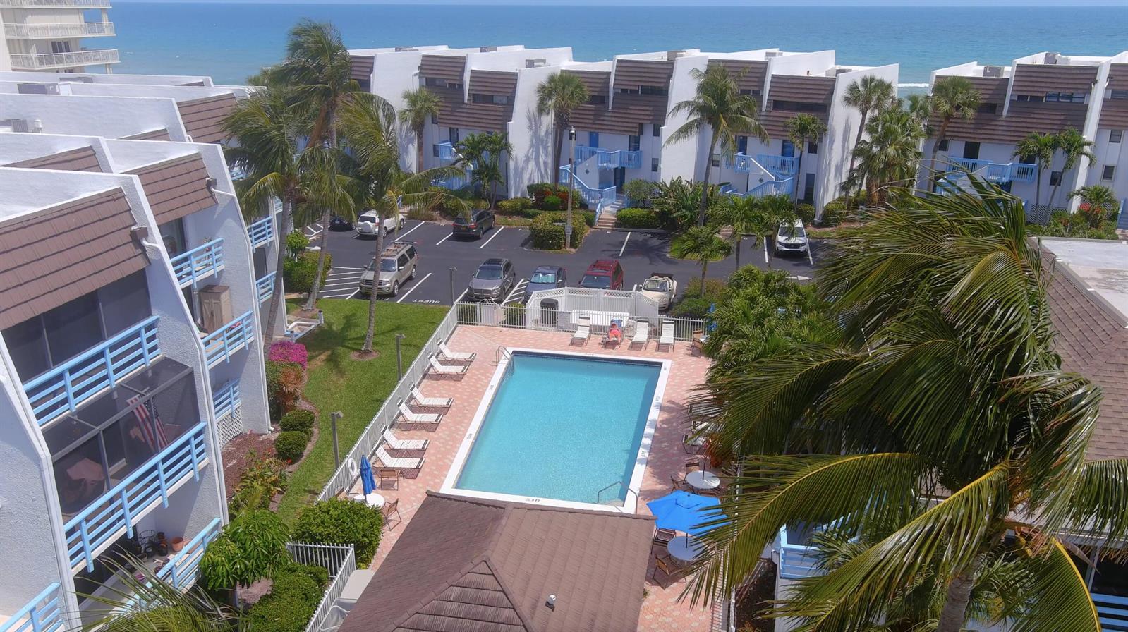 An aerial view of a swimming pool area surrounded by multi-story residential buildings and palm trees — 11000 S Ocean Drive # 6, Jensen Beach FL 34957, JENSEN BEACH, FL