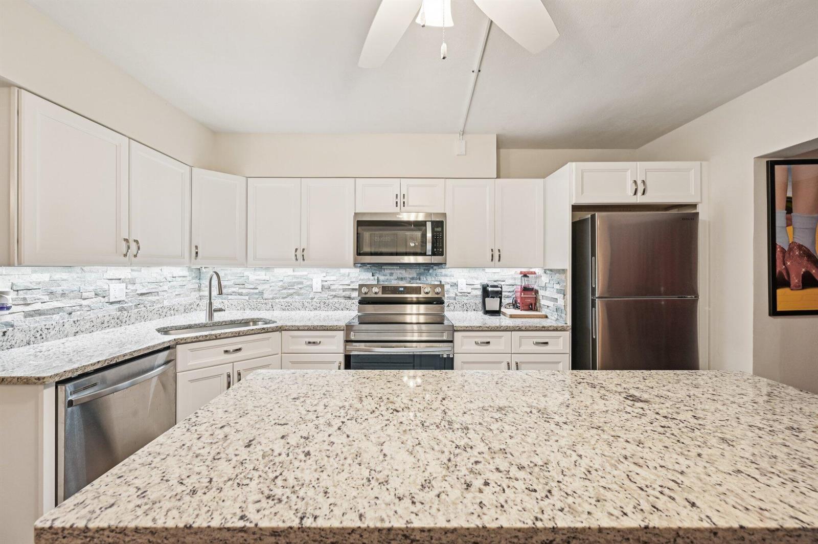 A kitchen features white cabinets, granite countertops, stainless steel appliances, and a stone tile backsplash — 11000 S Ocean Drive # 6, Jensen Beach FL 34957, JENSEN BEACH, FL