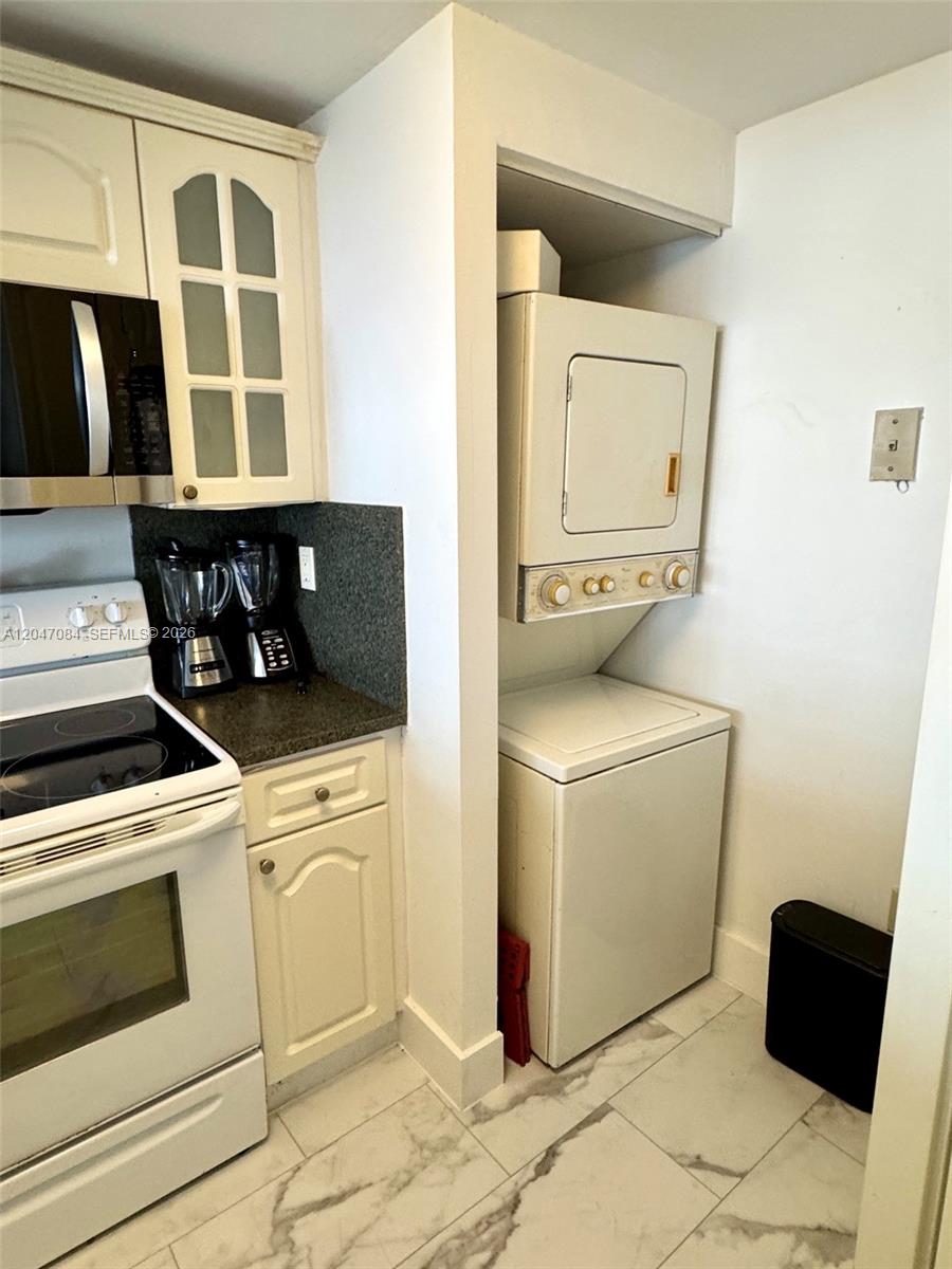 A kitchen features white cabinets, a stove, and a stacked washer and dryer unit — 600 NE 36th St # 609, Miami FL 33137, MIAMI, FL
