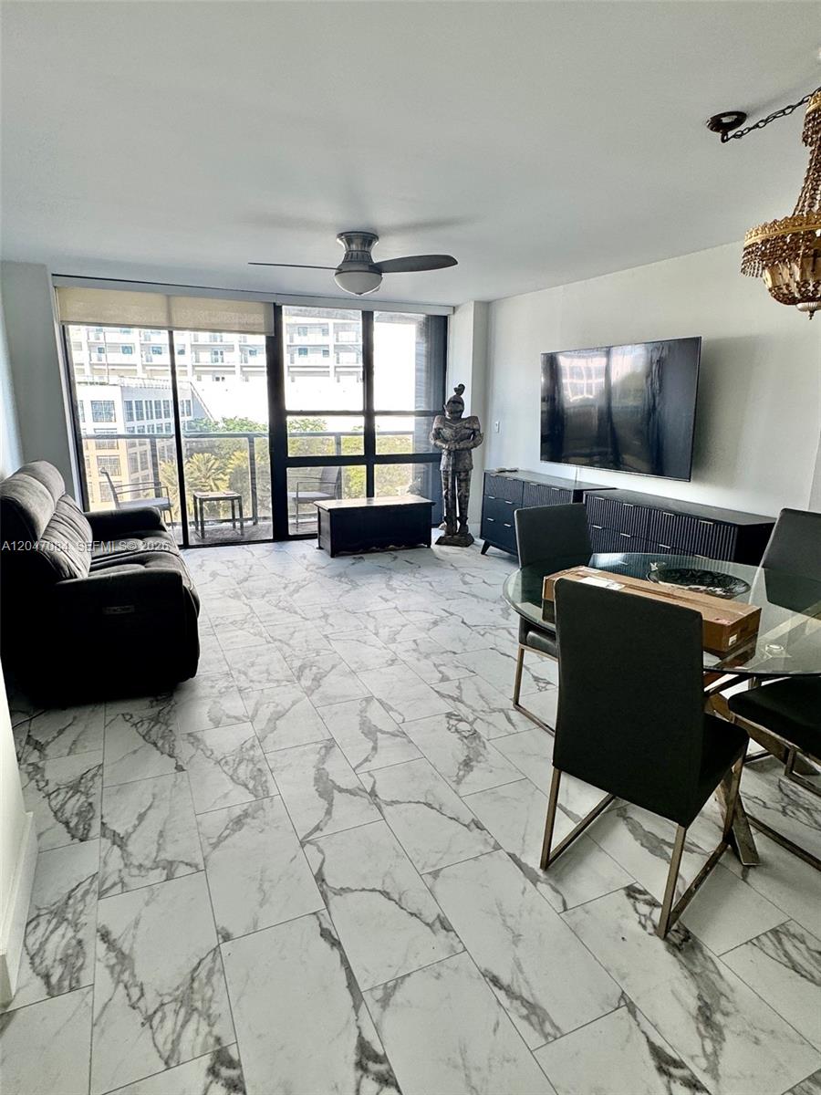 A living and dining room features marble-look tile flooring, a wall-mounted television, and balcony access — 600 NE 36th St # 609, Miami FL 33137, MIAMI, FL