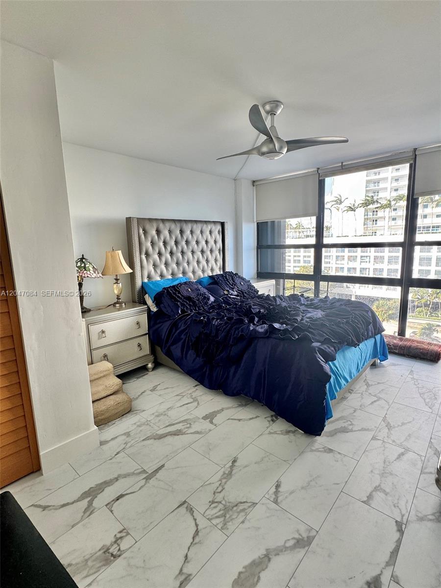 A bedroom features a tufted headboard, dark blue bedding, marble-look tile floors, and floor-to-ceiling windows — 600 NE 36th St # 609, Miami FL 33137, MIAMI, FL