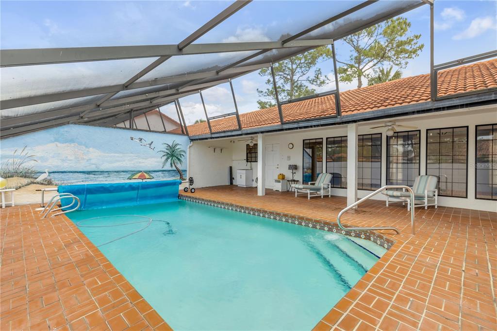 A screened-in swimming pool with a mural on the wall and a tiled patio area — 144 MARSH WREN COURT, DAYTONA BEACH, FL