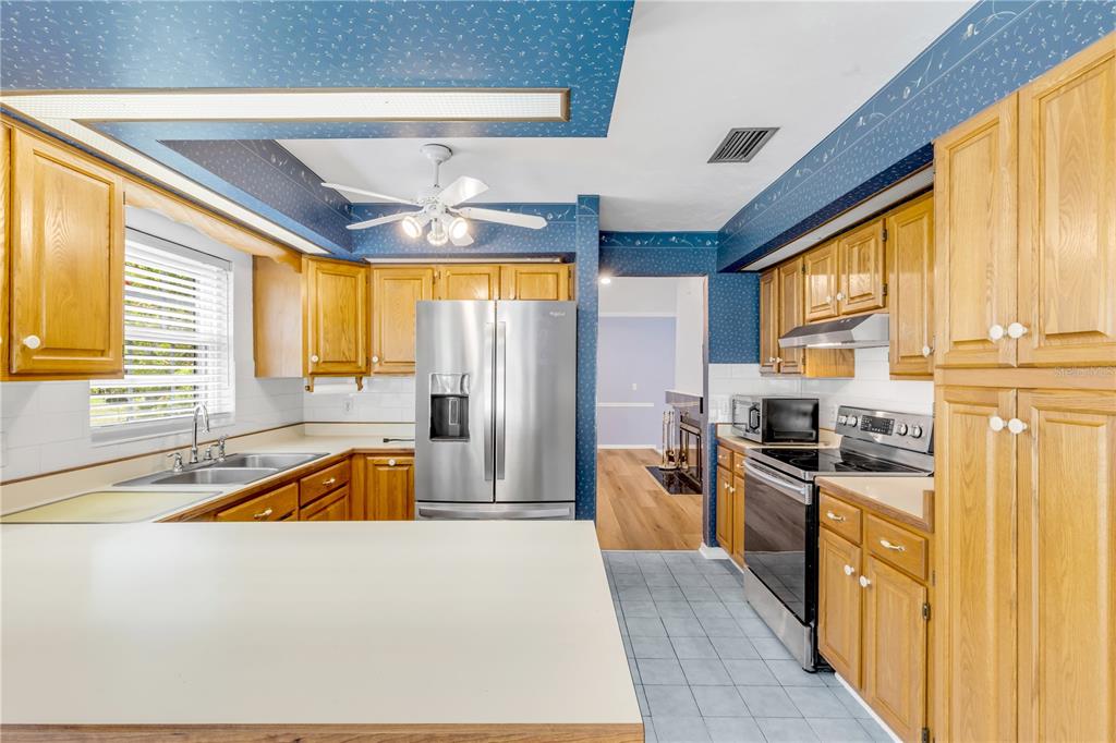 A kitchen features oak cabinets, stainless steel appliances, blue wallpaper, and a white countertop — 144 MARSH WREN COURT, DAYTONA BEACH, FL
