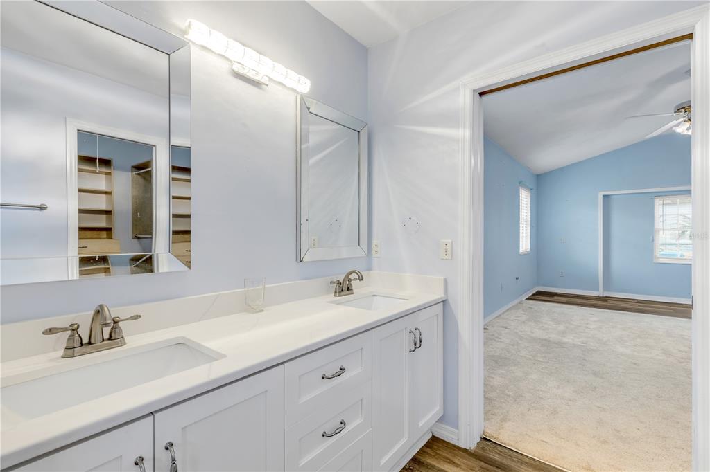 A bathroom with a double vanity and mirrors leads into a bedroom with blue walls — 144 MARSH WREN COURT, DAYTONA BEACH, FL