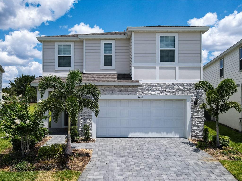 A two-story house with light siding, stone veneer, a two-car garage, and a paved driveway — 3401 LILAC WAY, DAVENPORT, FL