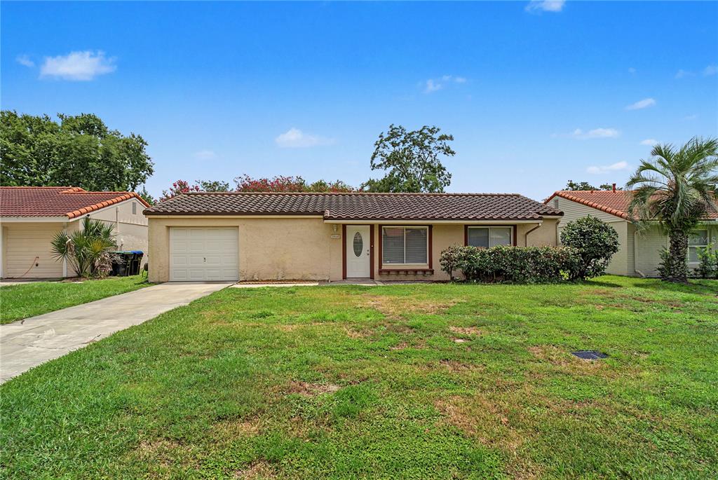 A single-story house with a tan stucco exterior, a tiled roof, and a front lawn — 10145 BLUFF COURT, ORLANDO, FL