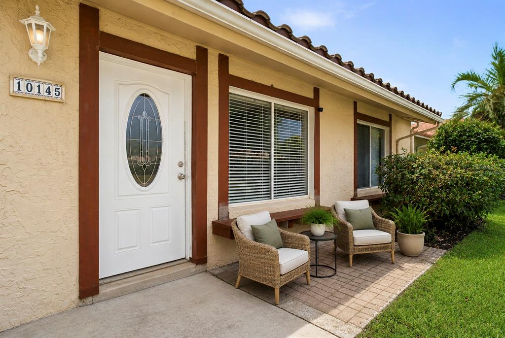 A white front door and two wicker chairs sit on a brick patio — 10145 BLUFF COURT, ORLANDO, FL