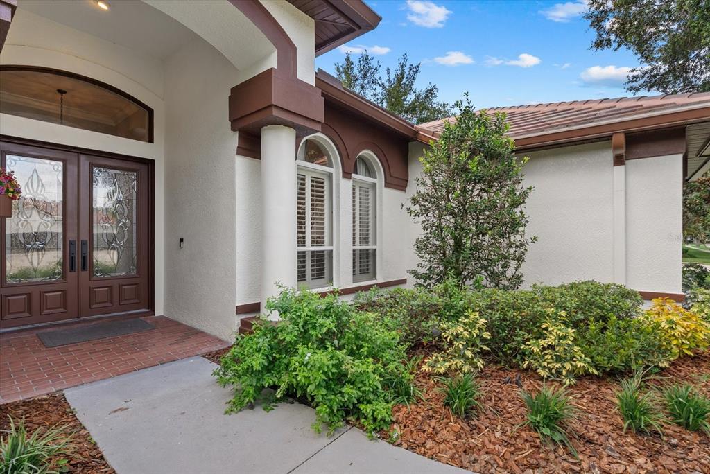 A front entrance with a double glass door, arched windows, and a landscaped garden bed — 9145 HIGHLAND RIDGE WAY, TAMPA, FL