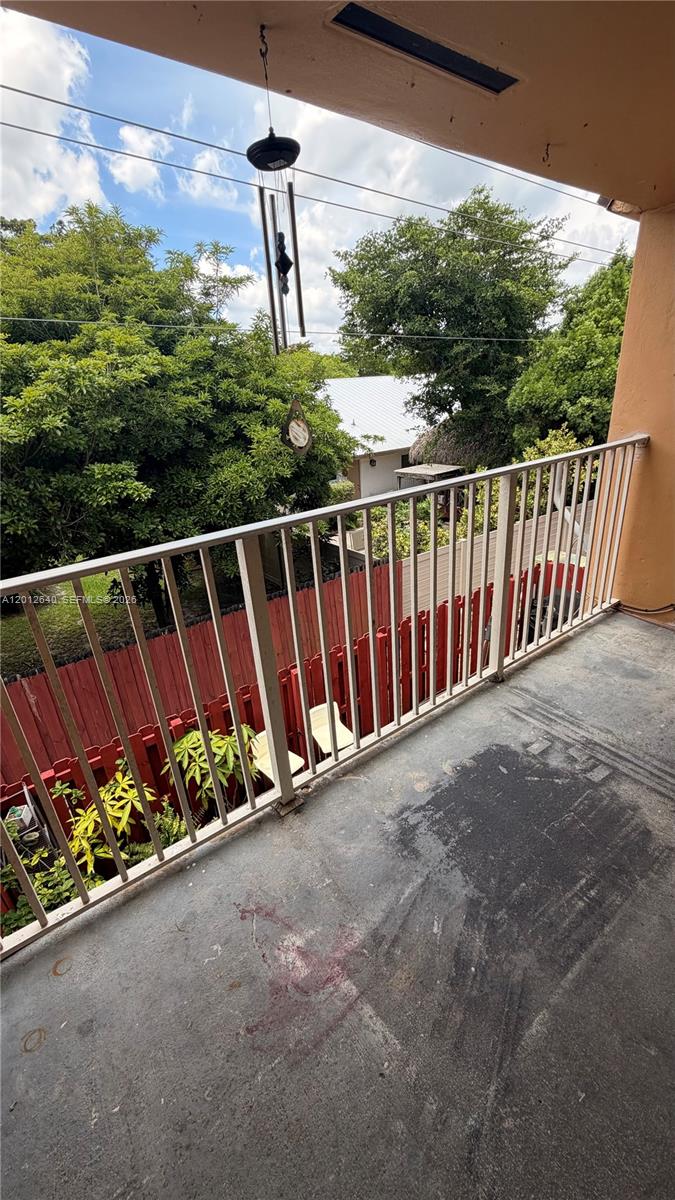 A balcony with a metal railing overlooks a yard with a red fence and trees — 9972 SW 88th St # 1125, Miami FL 33176, MIAMI, FL