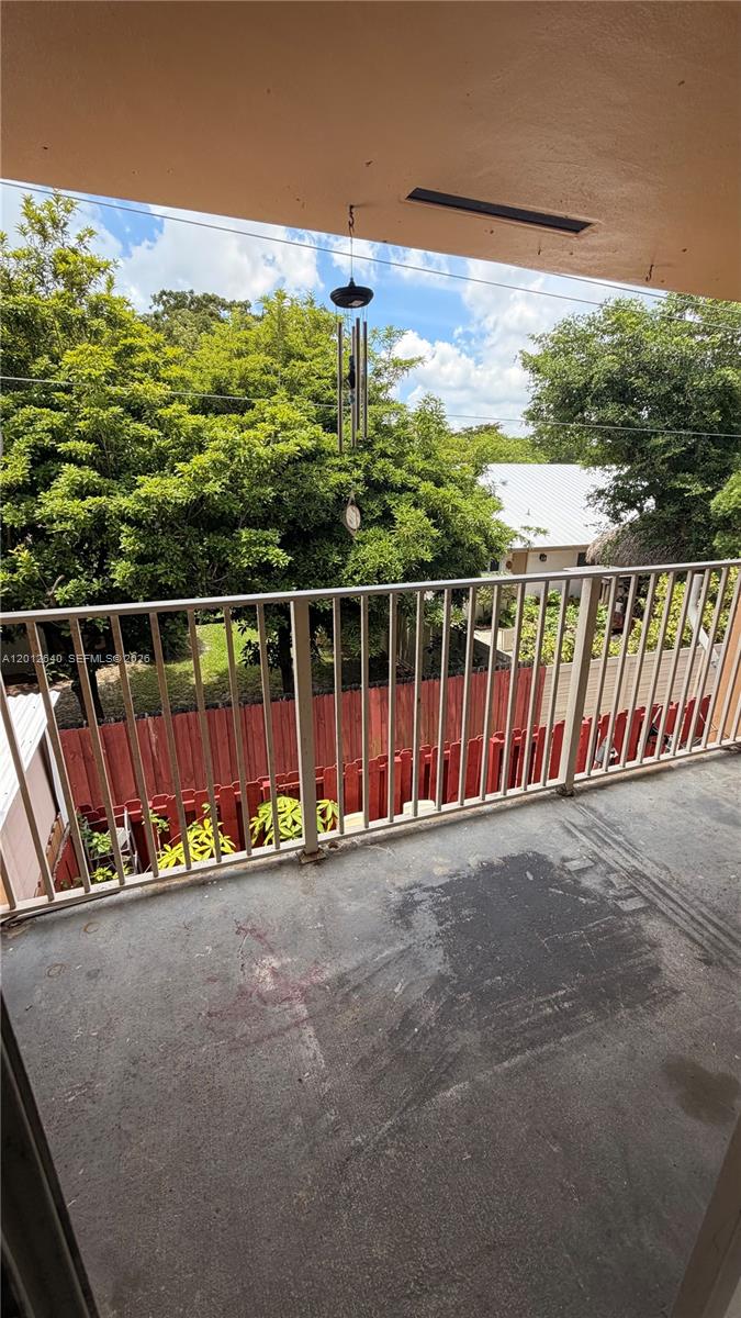 A balcony with a metal railing overlooks a backyard with a red fence and trees — 9972 SW 88th St # 1125, Miami FL 33176, MIAMI, FL
