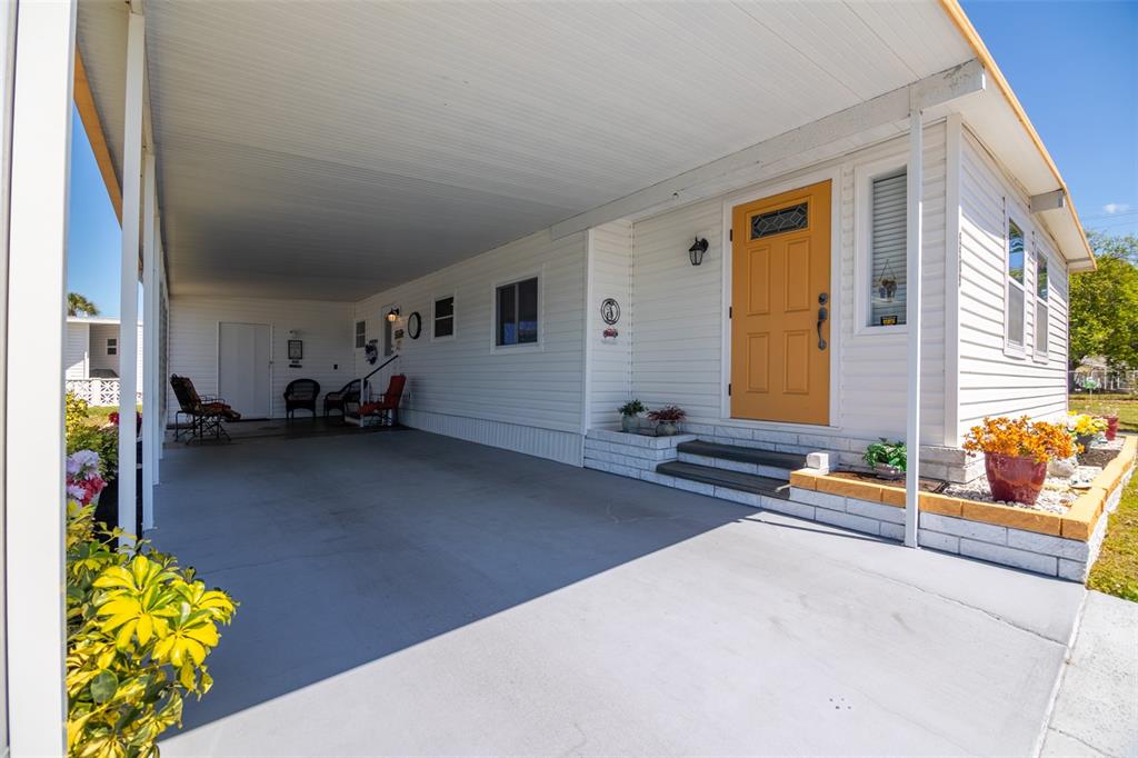 A white mobile home features a carport, a yellow front door, and a small garden — 5509 BERMUDA COURT, BRADENTON, FL
