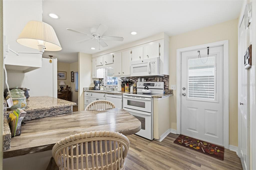 A kitchen features white cabinets, granite countertops, a dining table, and a white exterior door — 5509 BERMUDA COURT, BRADENTON, FL