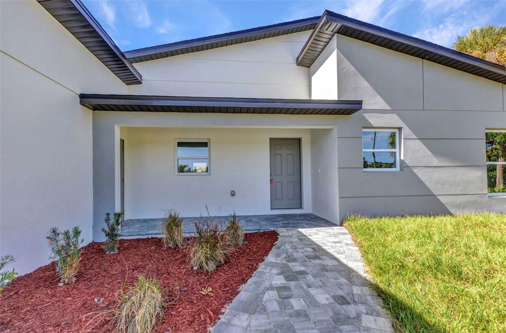 A modern house exterior features a gray door, stone walkway, and red mulch landscaping — 3435 W PRICE BOULEVARD, NORTH PORT, FL