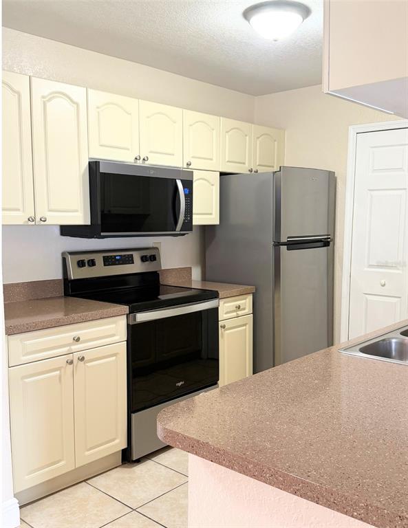 A kitchen features cream-colored cabinets, stainless steel appliances, and brown speckled countertops — 2550 N ALAFAYA TRAIL UNIT 6202, ORLANDO, FL