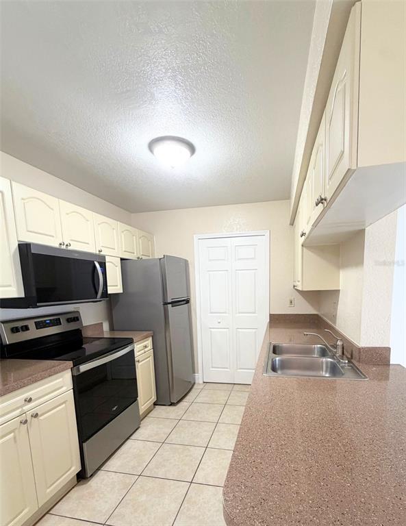 A kitchen features light-colored cabinets, stainless steel appliances, brown countertops, and tile flooring — 2550 N ALAFAYA TRAIL UNIT 6202, ORLANDO, FL