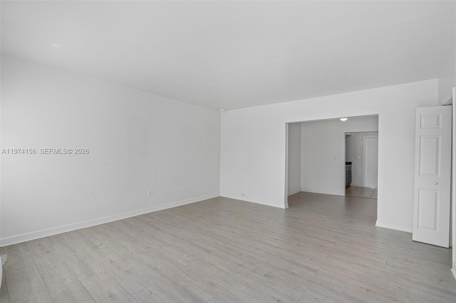 An empty room features white walls, light wood-look flooring, and an open doorway to another area — 8031 Hawthorne Ave, Miami Beach FL 33141, MIAMI BEACH, FL