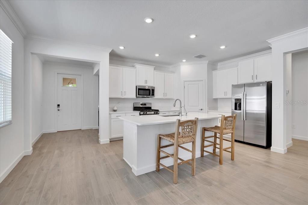 A modern white kitchen features a central island with bar stools and stainless steel appliances — 17410 HOLLY WELL AVENUE, WIMAUMA, FL