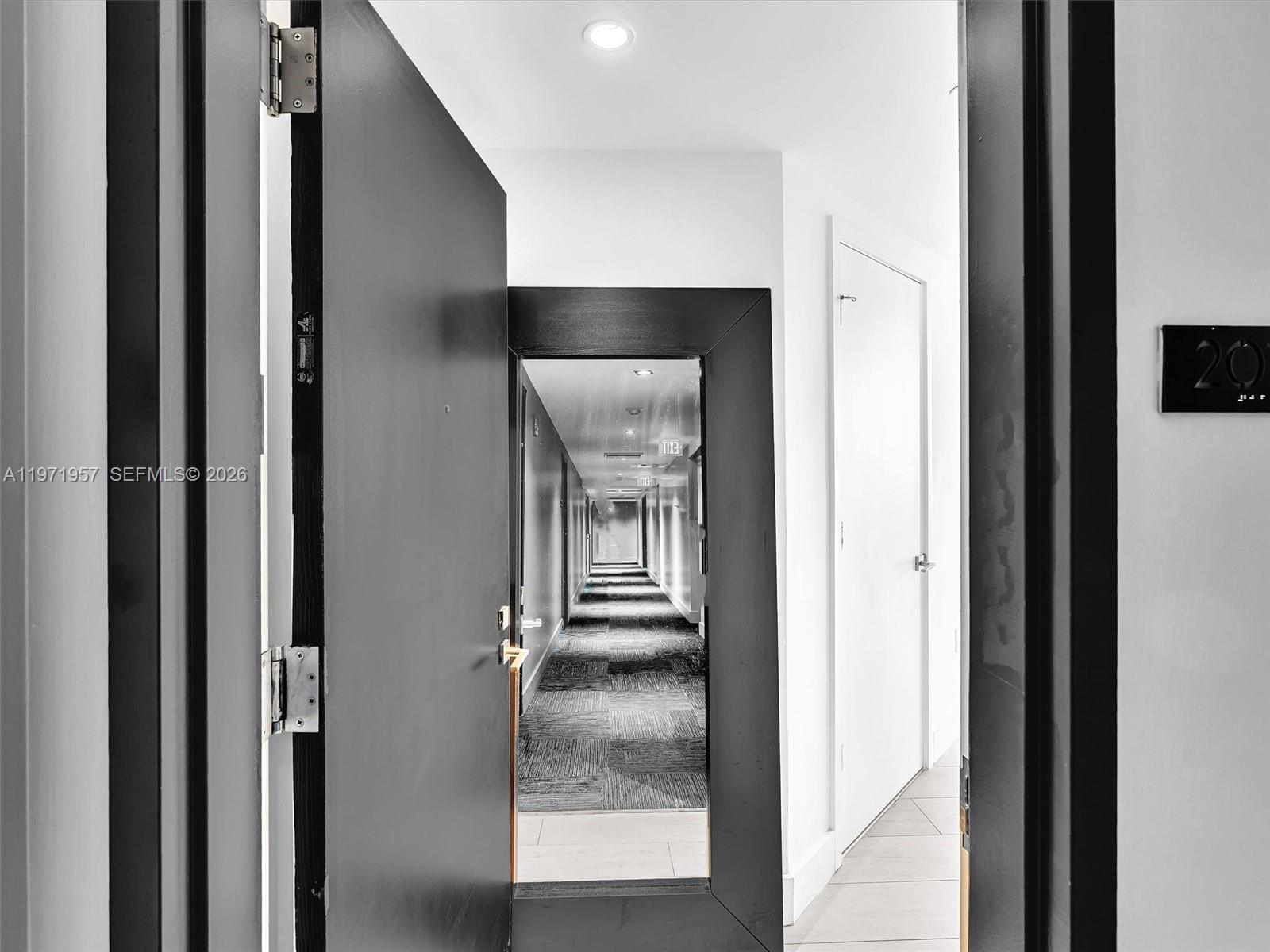 An open door reveals a long, narrow apartment building hallway with patterned carpeting — 121 NE 34th St # 2016, Miami FL 33137, MIAMI, FL