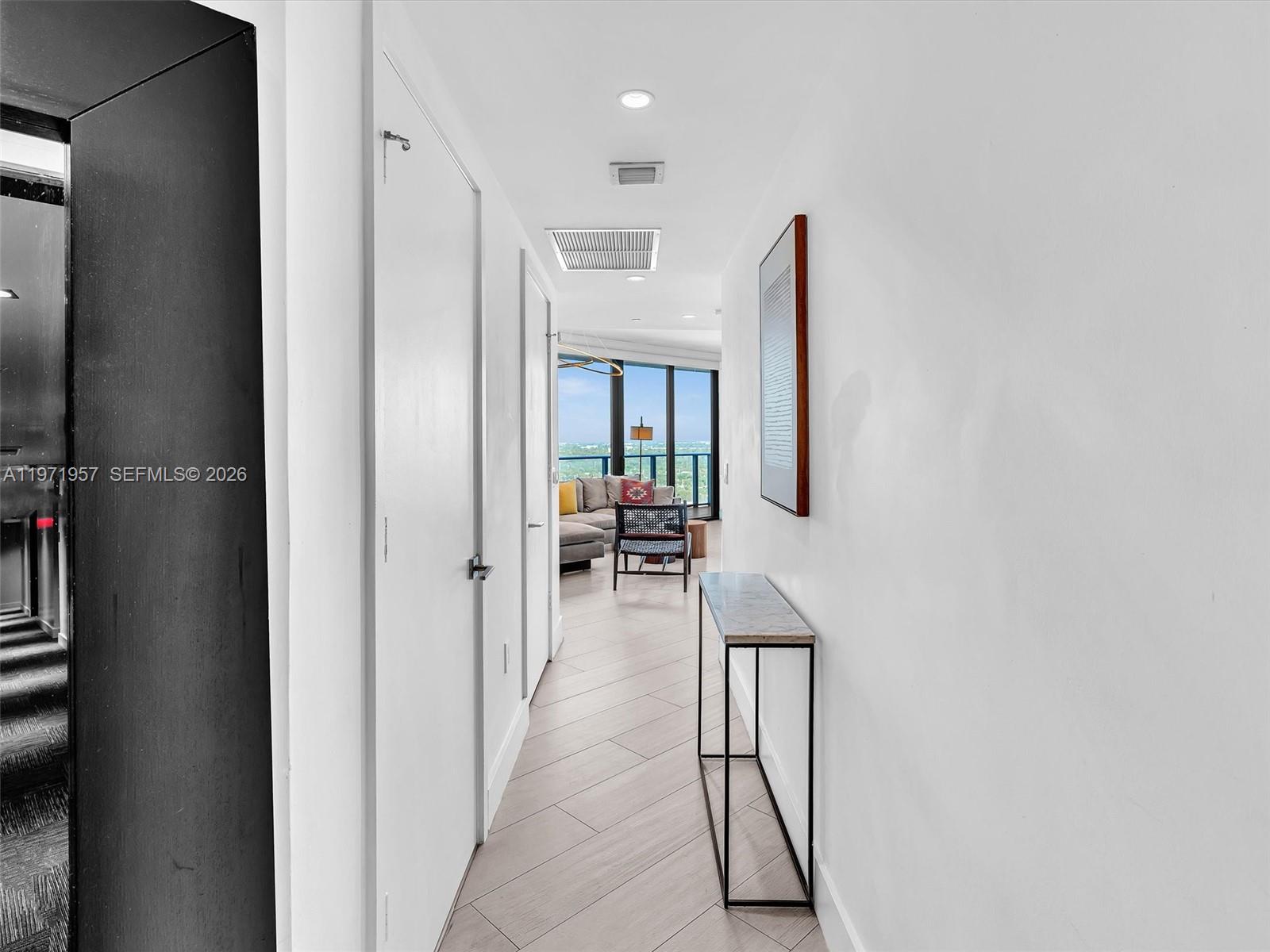 A hallway with light wood floors leads to a living area with floor-to-ceiling windows — 121 NE 34th St # 2016, Miami FL 33137, MIAMI, FL