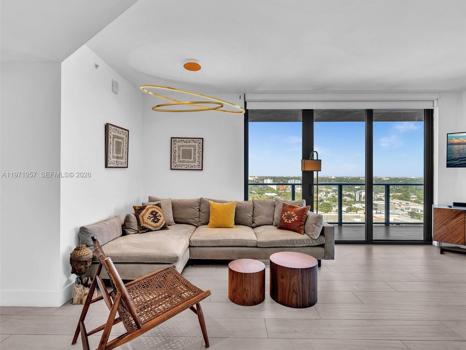 A living room features a sectional sofa, wooden coffee tables, and floor-to-ceiling windows with views — 121 NE 34th St # 2016, Miami FL 33137, MIAMI, FL