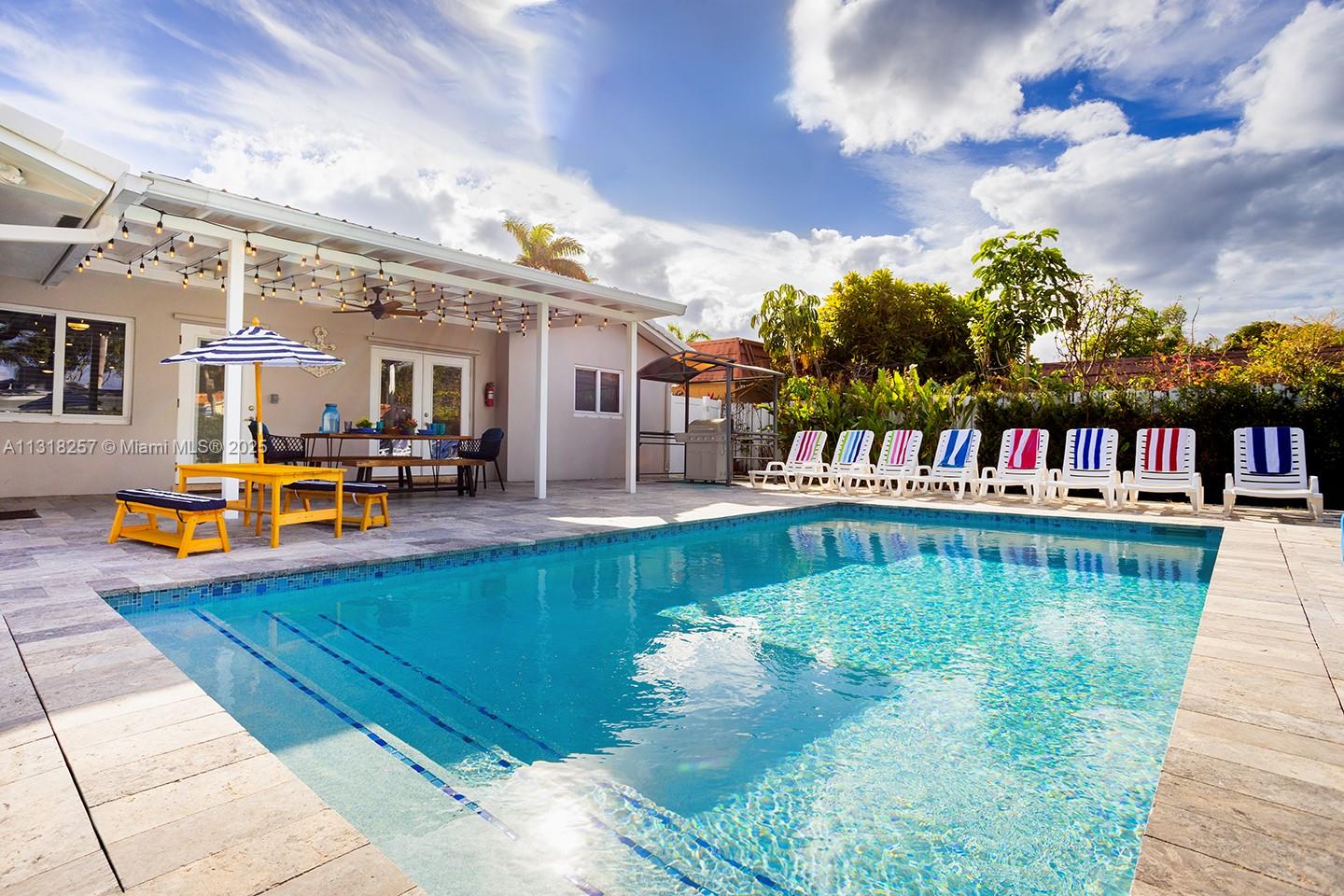 A backyard swimming pool features a covered patio, outdoor dining area, and multiple lounge chairs — 833 Washington St, Hollywood FL 33019, HOLLYWOOD, FL