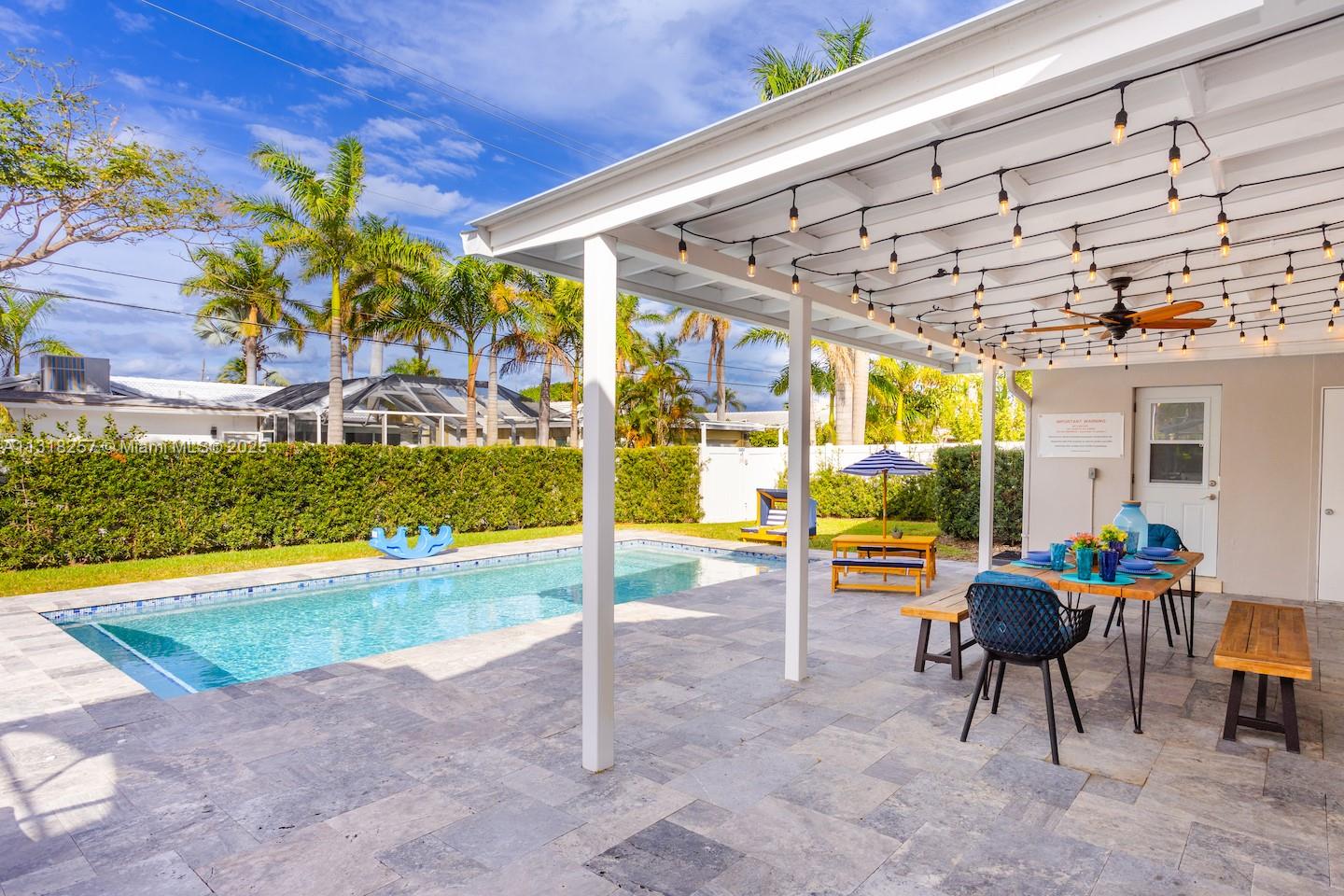 A backyard patio features a swimming pool, a dining area, and string lights under a pergola — 833 Washington St, Hollywood FL 33019, HOLLYWOOD, FL