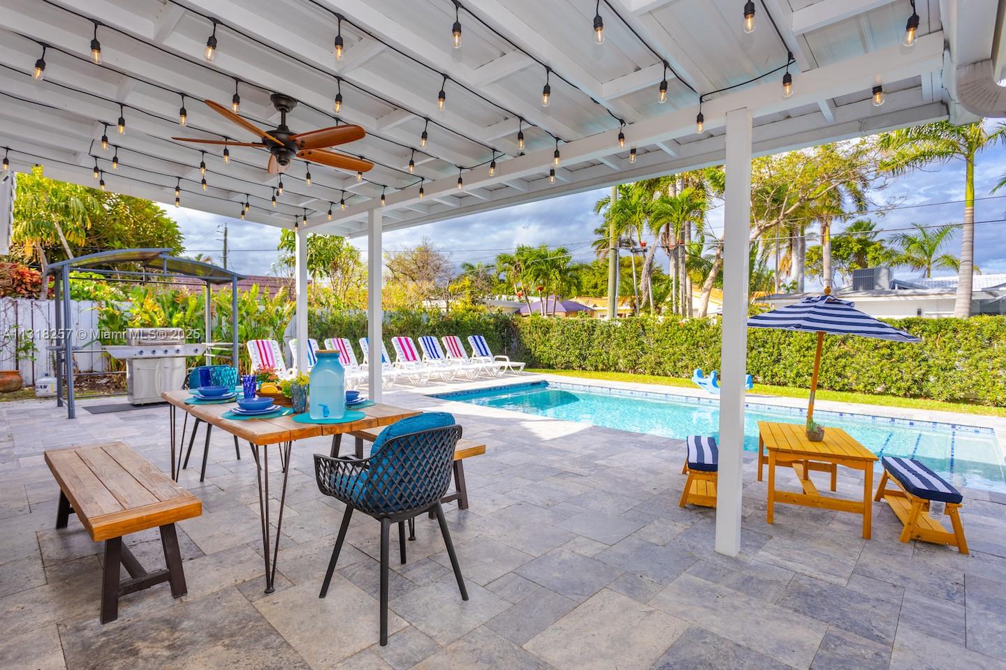A covered patio features a dining set, a swimming pool, and lounge chairs in a backyard — 833 Washington St, Hollywood FL 33019, HOLLYWOOD, FL