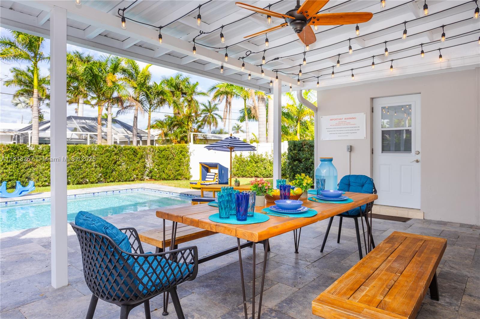 A covered outdoor patio features a wooden dining table, benches, and a swimming pool — 833 Washington St, Hollywood FL 33019, HOLLYWOOD, FL