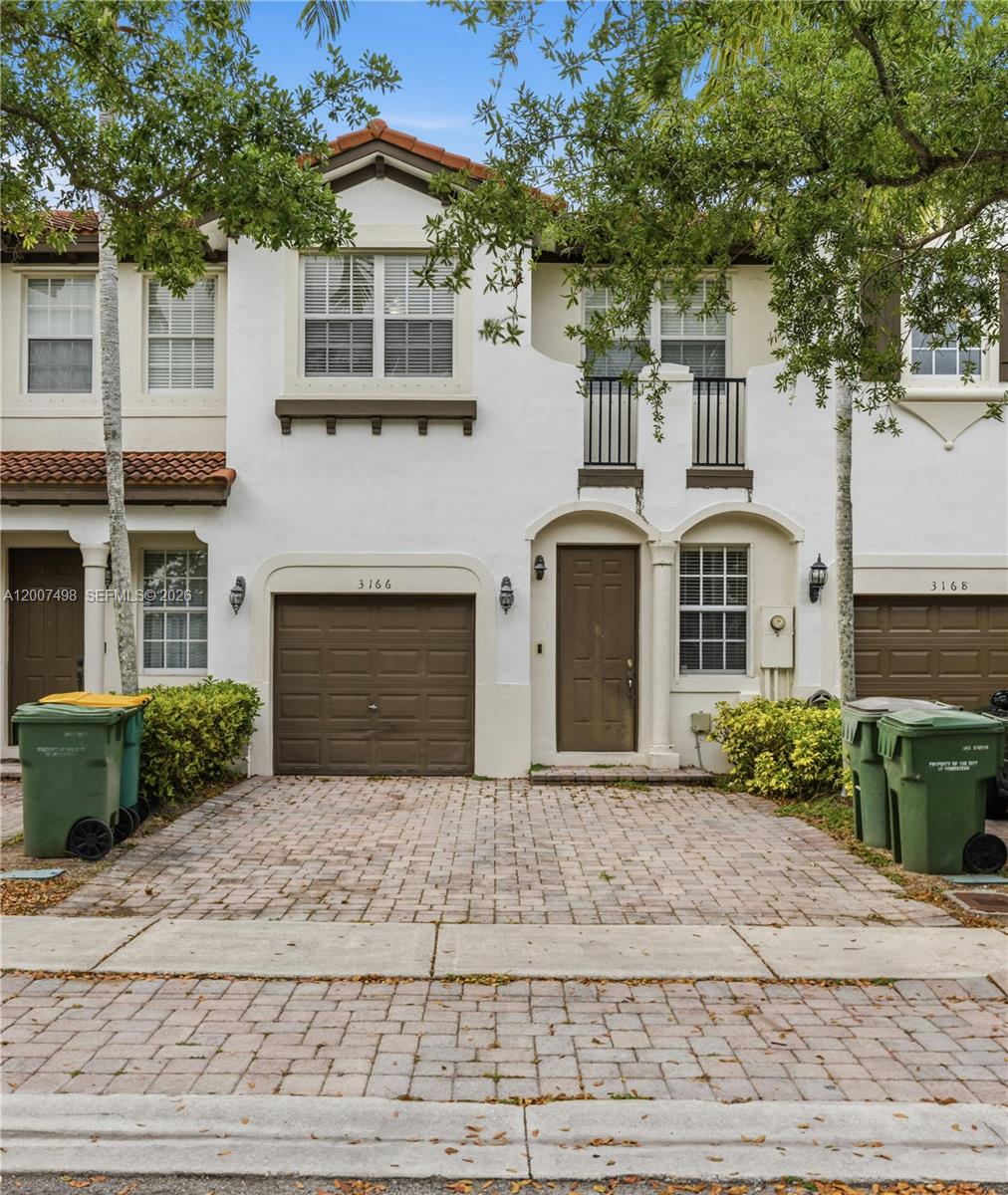 A two-story townhouse exterior features a brown garage door, a front entrance, and a paved driveway — 3166 NE 11th St, Homestead FL 33033, HOMESTEAD, FL