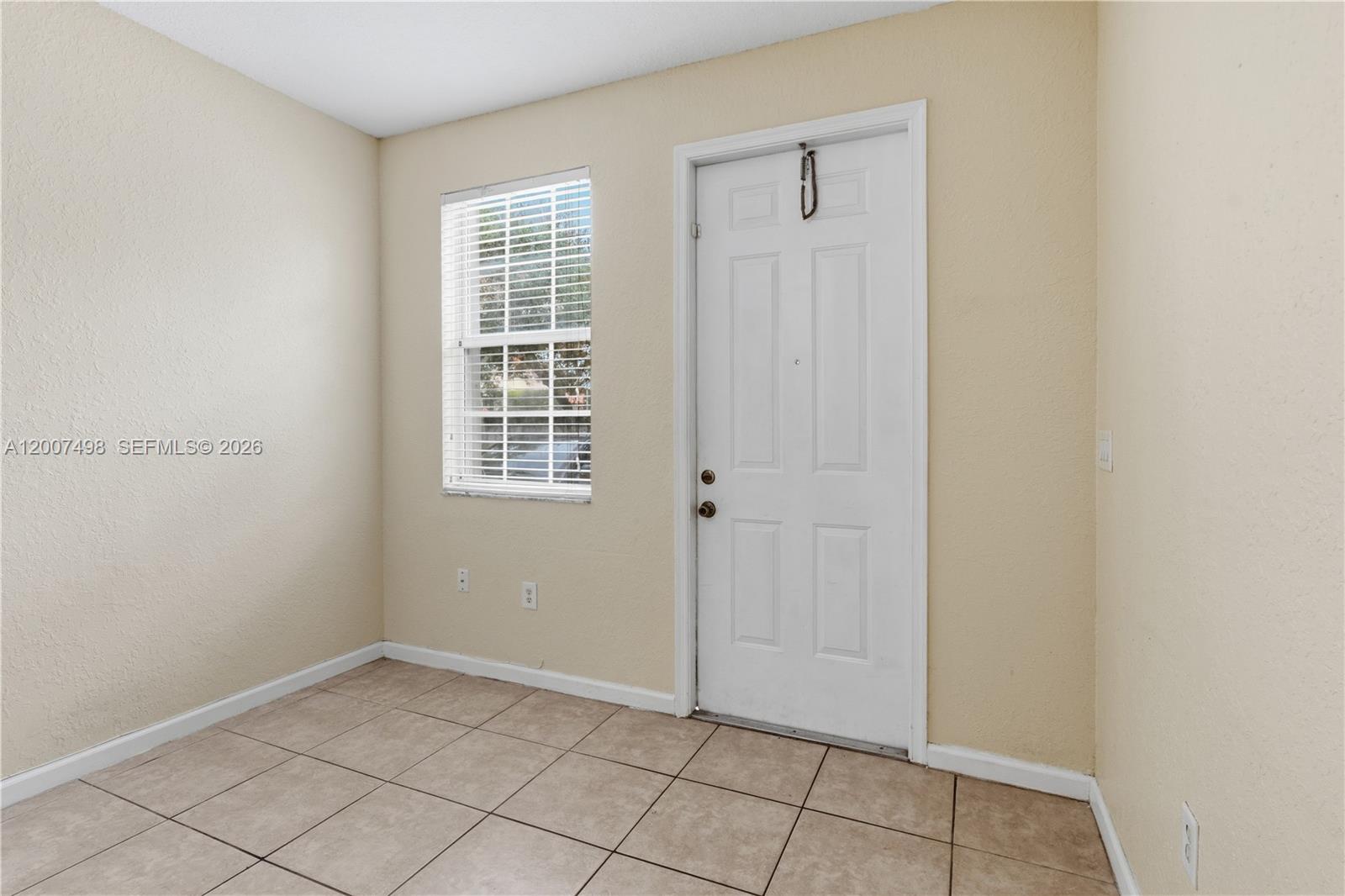 A small room with beige walls, tile flooring, a single window, and a white door — 3166 NE 11th St, Homestead FL 33033, HOMESTEAD, FL