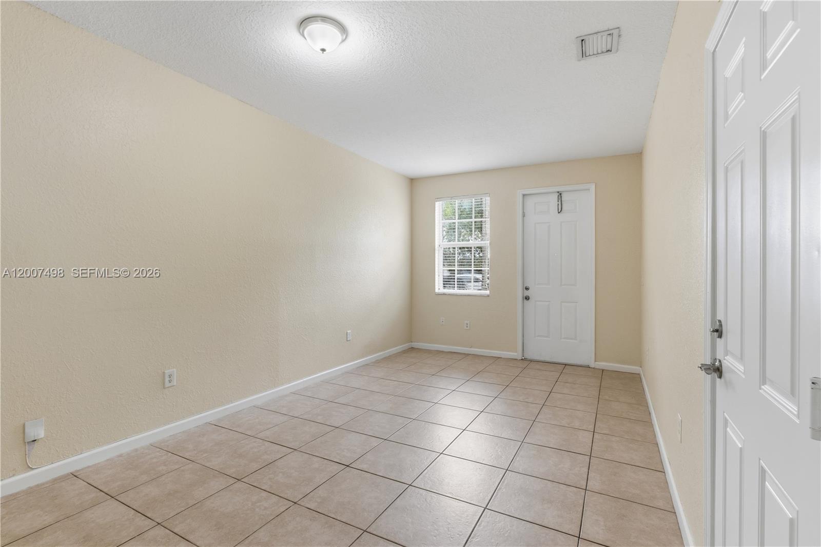 An empty room features beige walls, light-colored tile flooring, a window, and a white door — 3166 NE 11th St, Homestead FL 33033, HOMESTEAD, FL