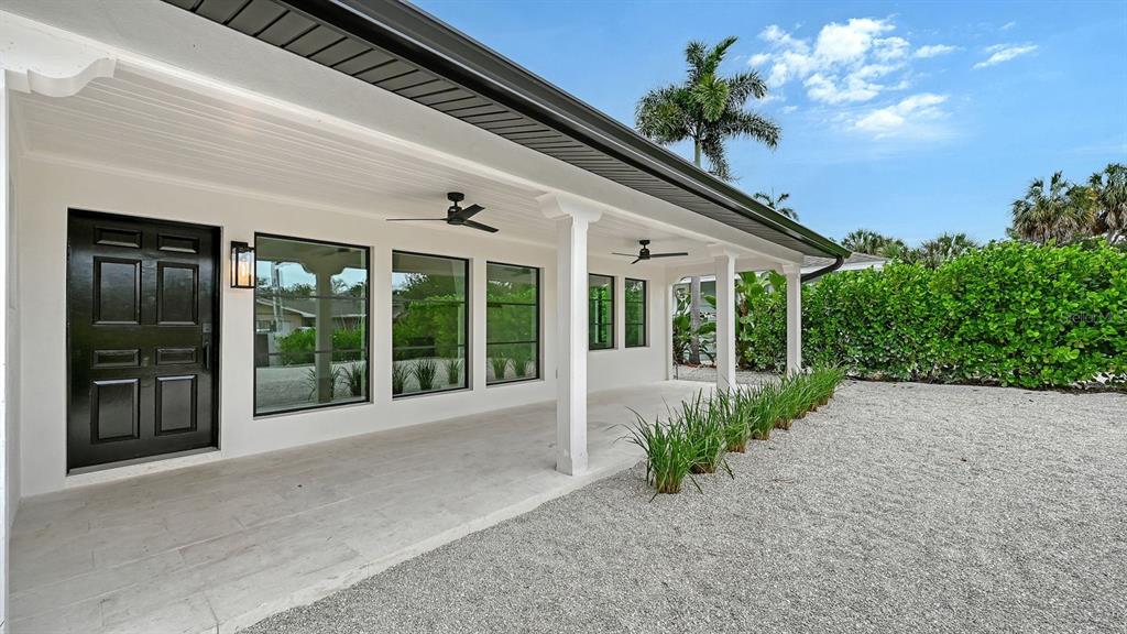 A covered patio with white columns, ceiling fans, and large windows overlooks a gravel yard — 1041 INDIAN BEACH DRIVE, SARASOTA, FL