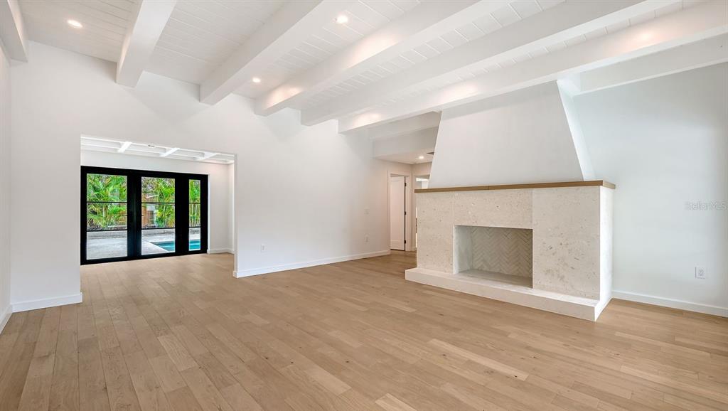 A living room features a vaulted ceiling with exposed beams, light wood floors, and a fireplace — 1041 INDIAN BEACH DRIVE, SARASOTA, FL