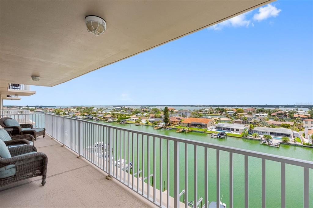 A balcony with wicker chairs overlooks a canal and residential neighborhood under a blue sky — 223 ISLAND WAY UNIT 7F, CLEARWATER BEACH, FL
