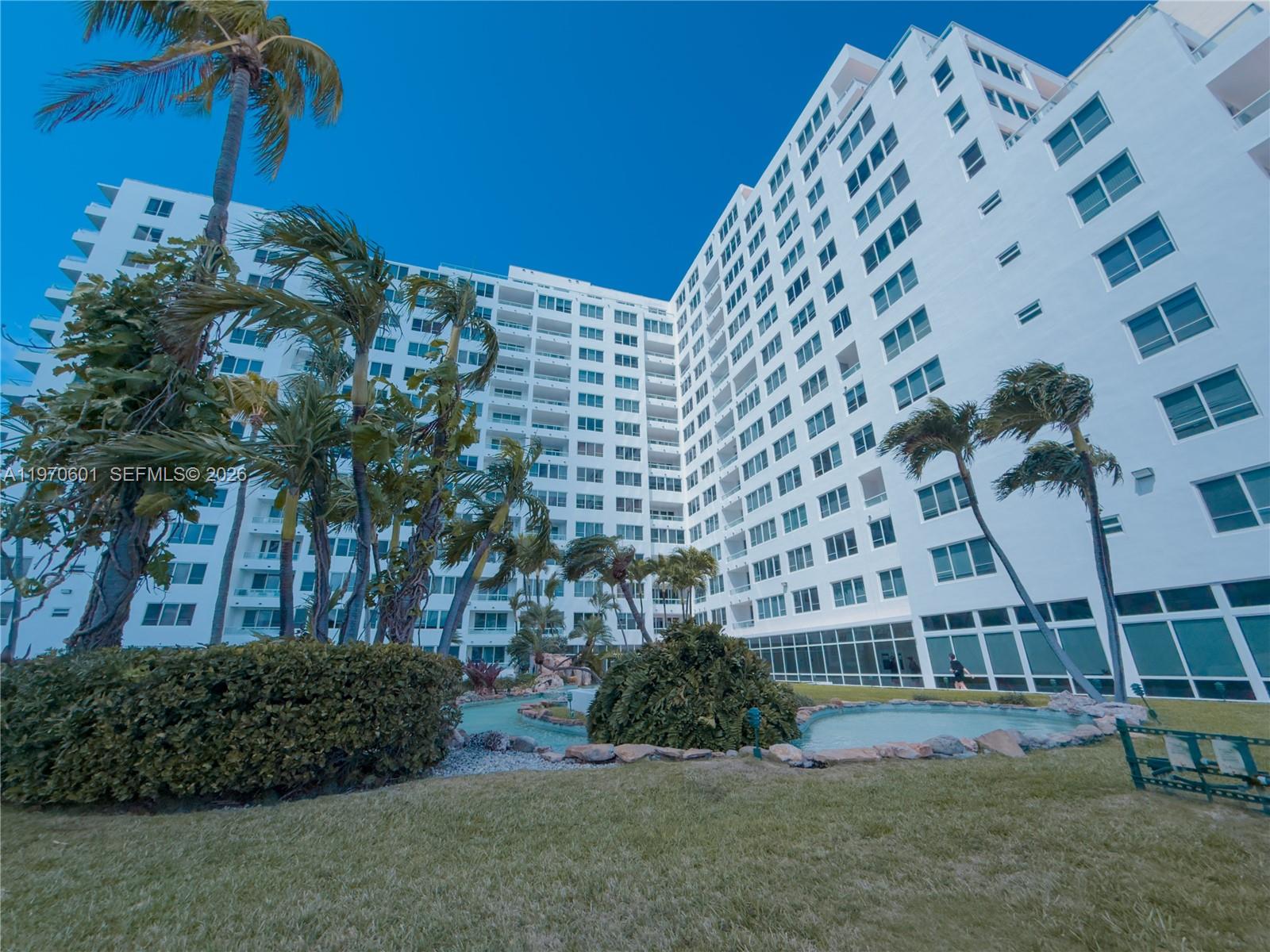 A low-angle view of a white multi-story apartment building with palm trees and landscaping — 5005 Collins Ave # 825, Miami Beach FL 33140, MIAMI BEACH, FL