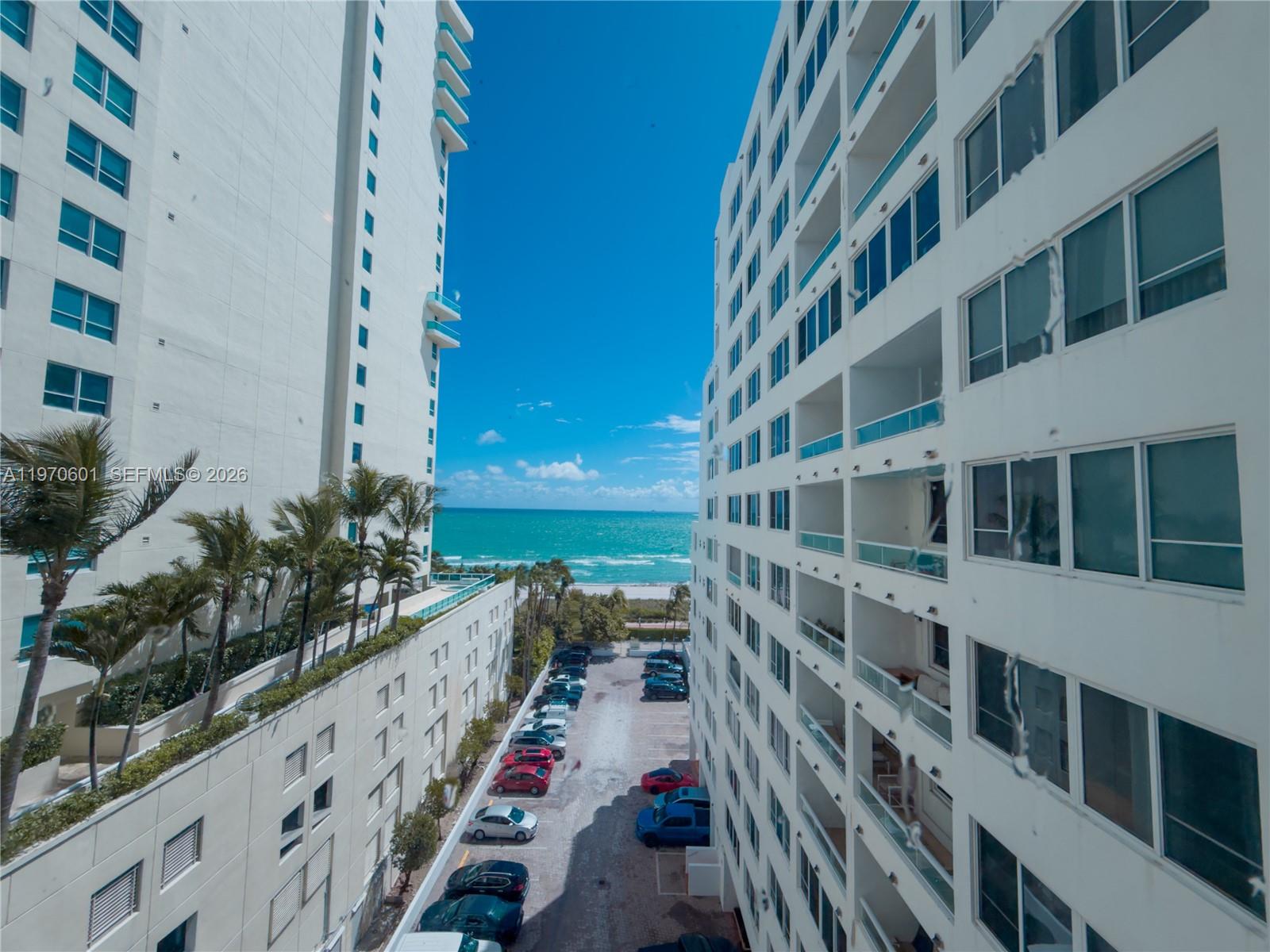 An exterior view shows two tall residential buildings flanking a parking lot leading to the ocean — 5005 Collins Ave # 825, Miami Beach FL 33140, MIAMI BEACH, FL