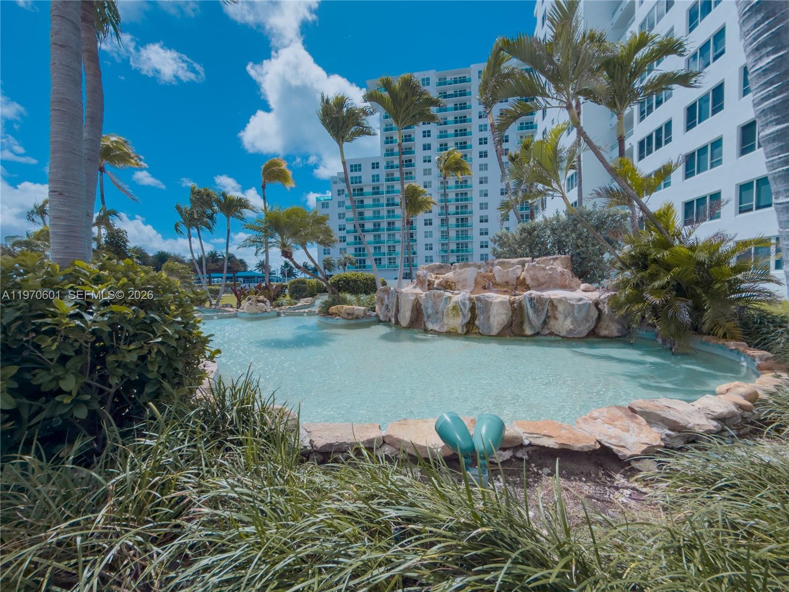 A landscaped pool area with a rock waterfall feature sits in front of a high-rise building — 5005 Collins Ave # 825, Miami Beach FL 33140, MIAMI BEACH, FL