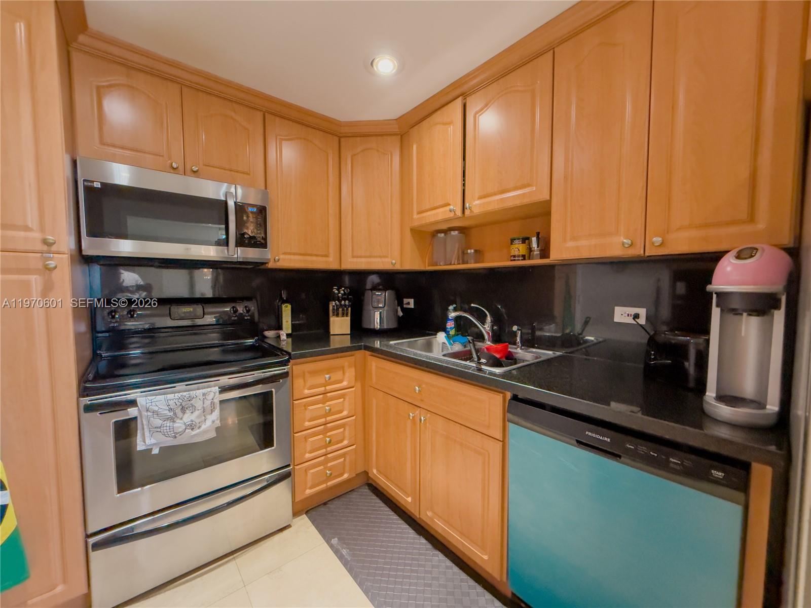 A kitchen features light wood cabinets, black countertops, stainless steel appliances, and a teal dishwasher — 5005 Collins Ave # 825, Miami Beach FL 33140, MIAMI BEACH, FL
