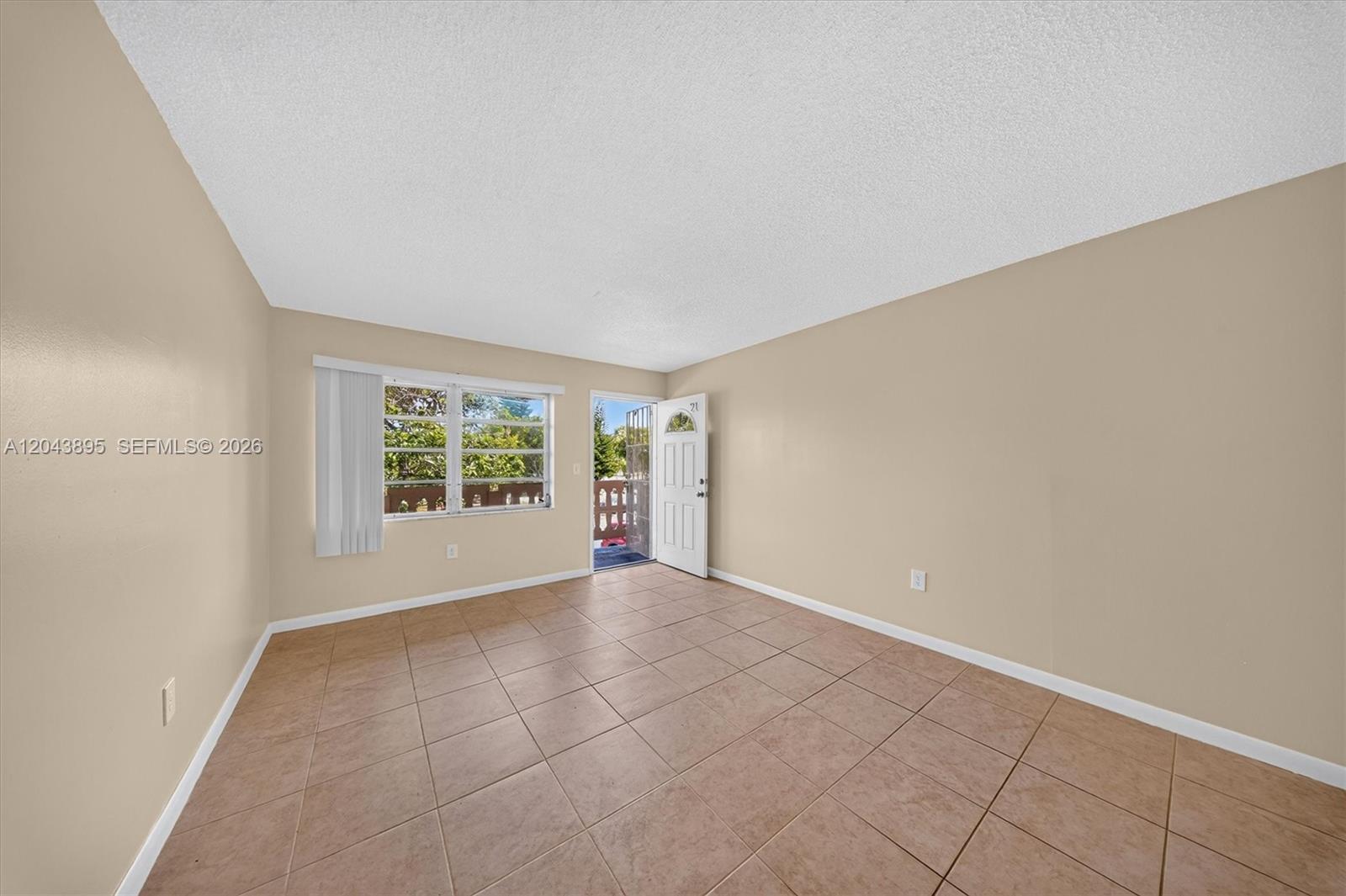 An empty room features beige walls, light-colored tile flooring, a window, and an open door — 20311 NE 2nd Ave # 21, Miami FL 33179, MIAMI, FL